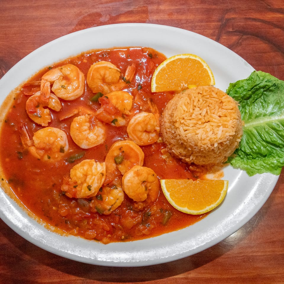 Shrimp in red sauce with rice, orange slices, and lettuce on a white plate.