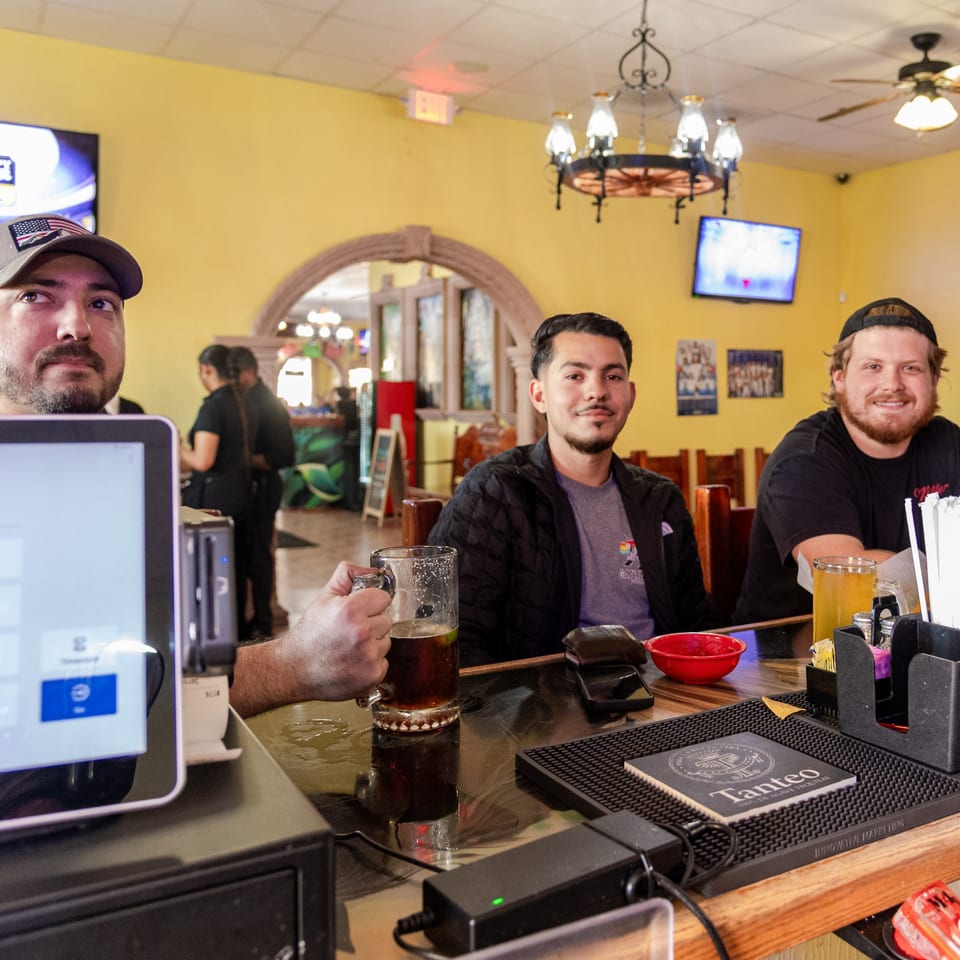 Three men at a bar counter, one holding a beer, inside Mi Mexico Restaurant.