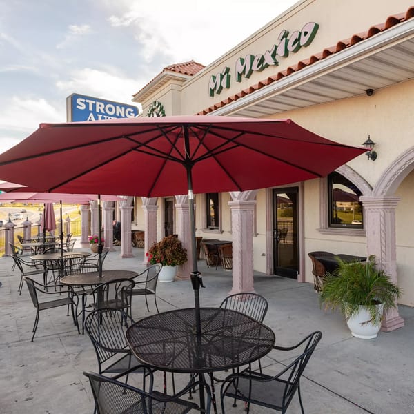 Outdoor patio of Mi Mexico Restaurant with red umbrellas, black tables, and chairs.