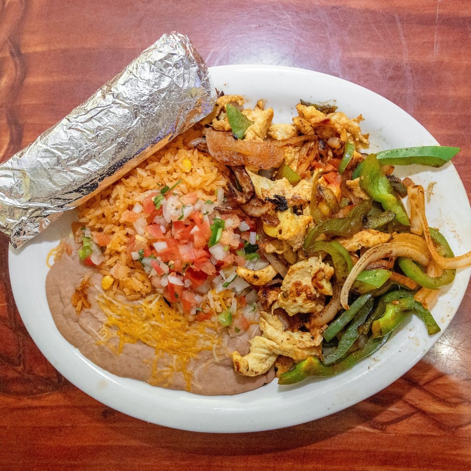 Mi Mexico Restaurant's fajita plate with chicken, peppers, onions, rice, beans, pico de gallo, and a foil-wrapped burrito.