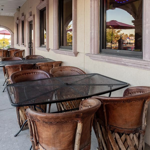 Outdoor patio seating at Mi Mexico Restaurant with brown leather chairs and black mesh tables.