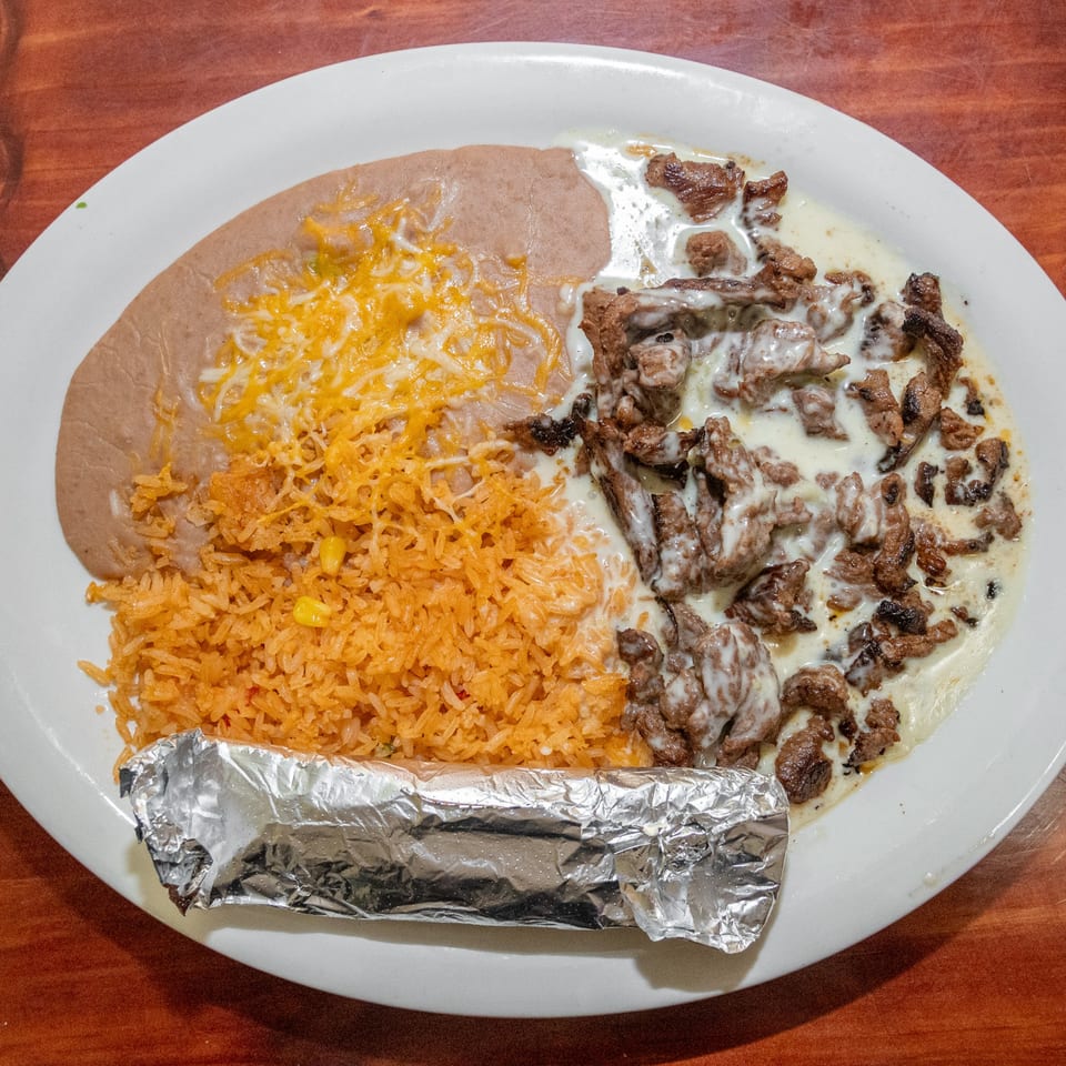 Mi Mexico's Mexican dish with steak in white sauce, refried beans with cheese, rice, and a foil-wrapped item.