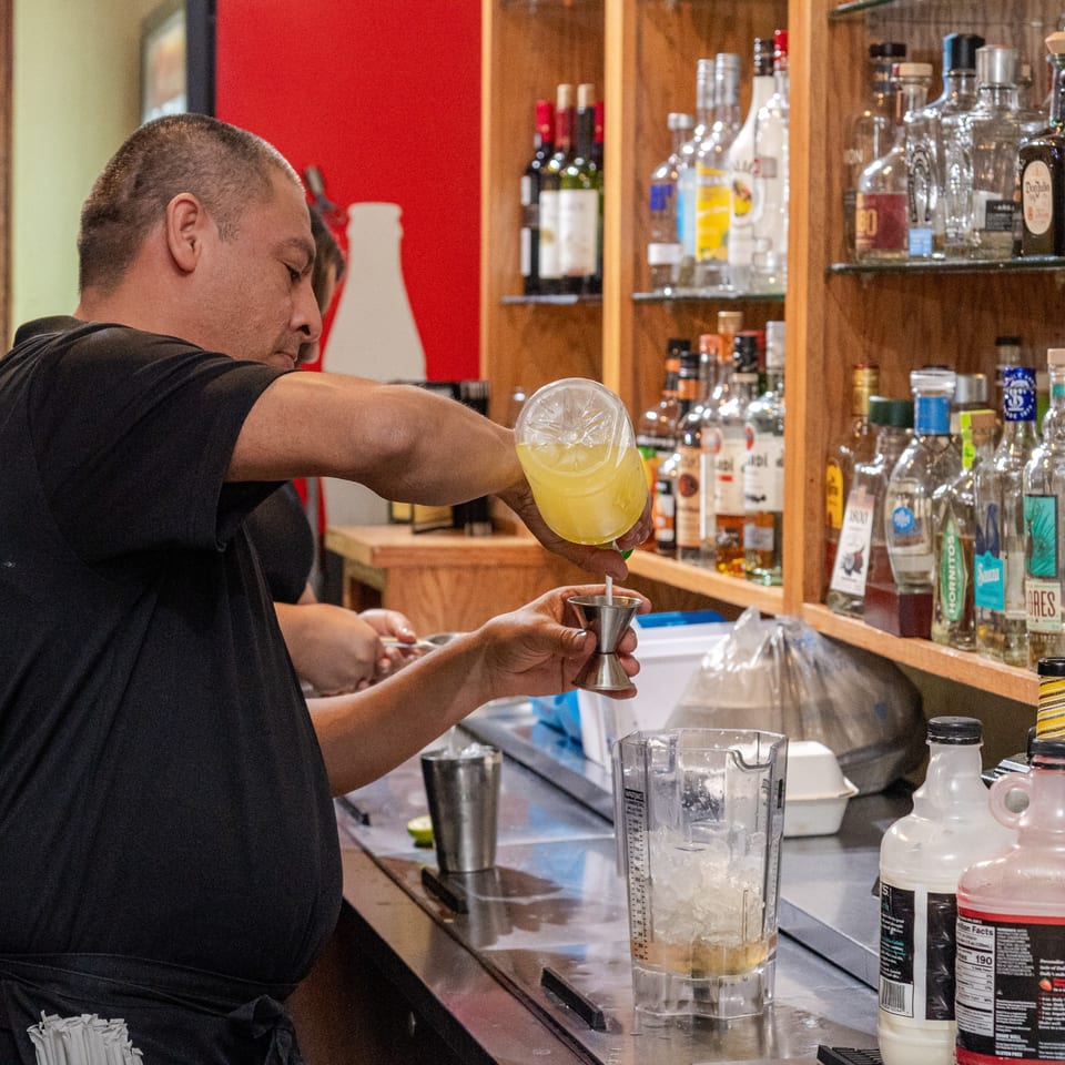 A bartender at Mi Mexico Restaurant pours a yellow liquid from a bottle into a jigger.