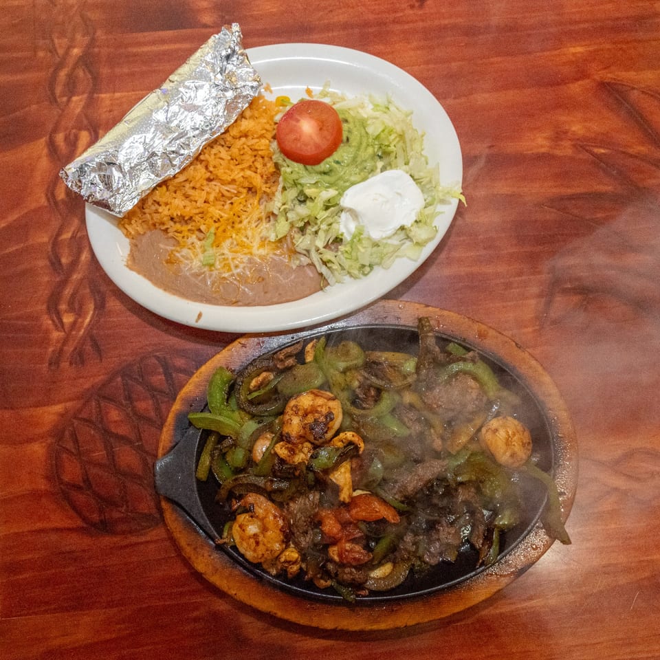 Sizzling fajitas with shrimp, steak, and vegetables, alongside a plate of rice, beans, and salad.