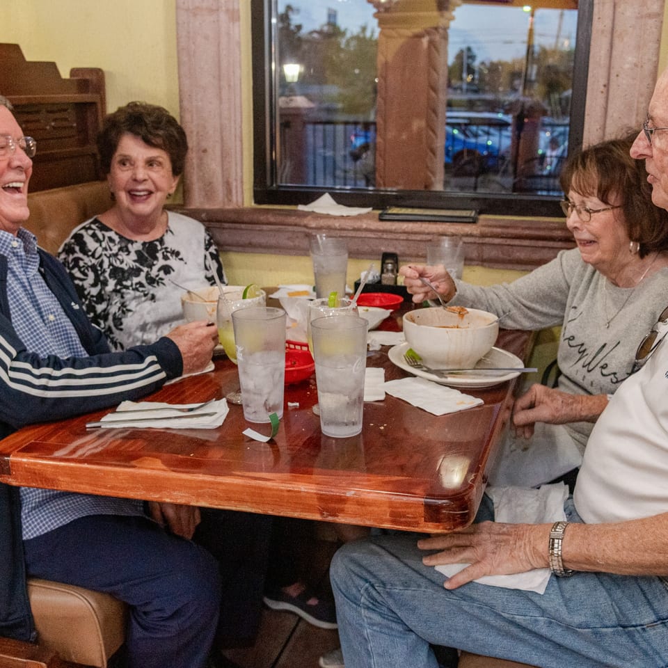 Four happy customers enjoying a meal together at Mi Mexico Restaurant, with drinks and food on the table.