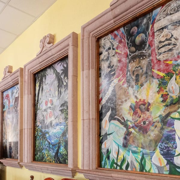 Three framed paintings on a yellow wall, depicting Mexican cultural and historical scenes.