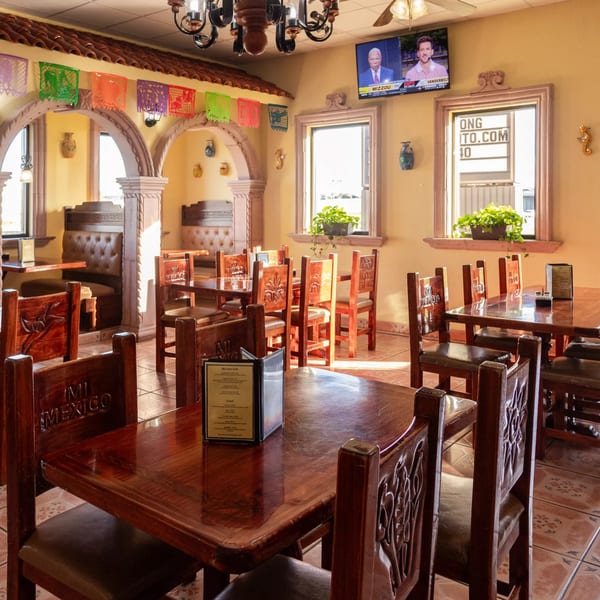 Mi Mexico Restaurant interior with wooden tables and chairs, arched doorways, and colorful papel picado decorations.